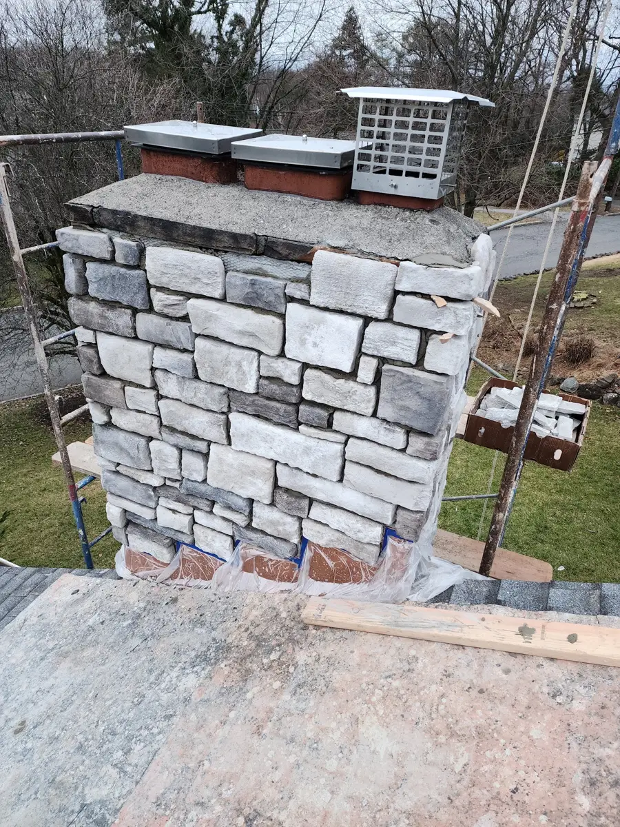 Stone chimney with concrete crown and metal caps photographed from roof scaffolding