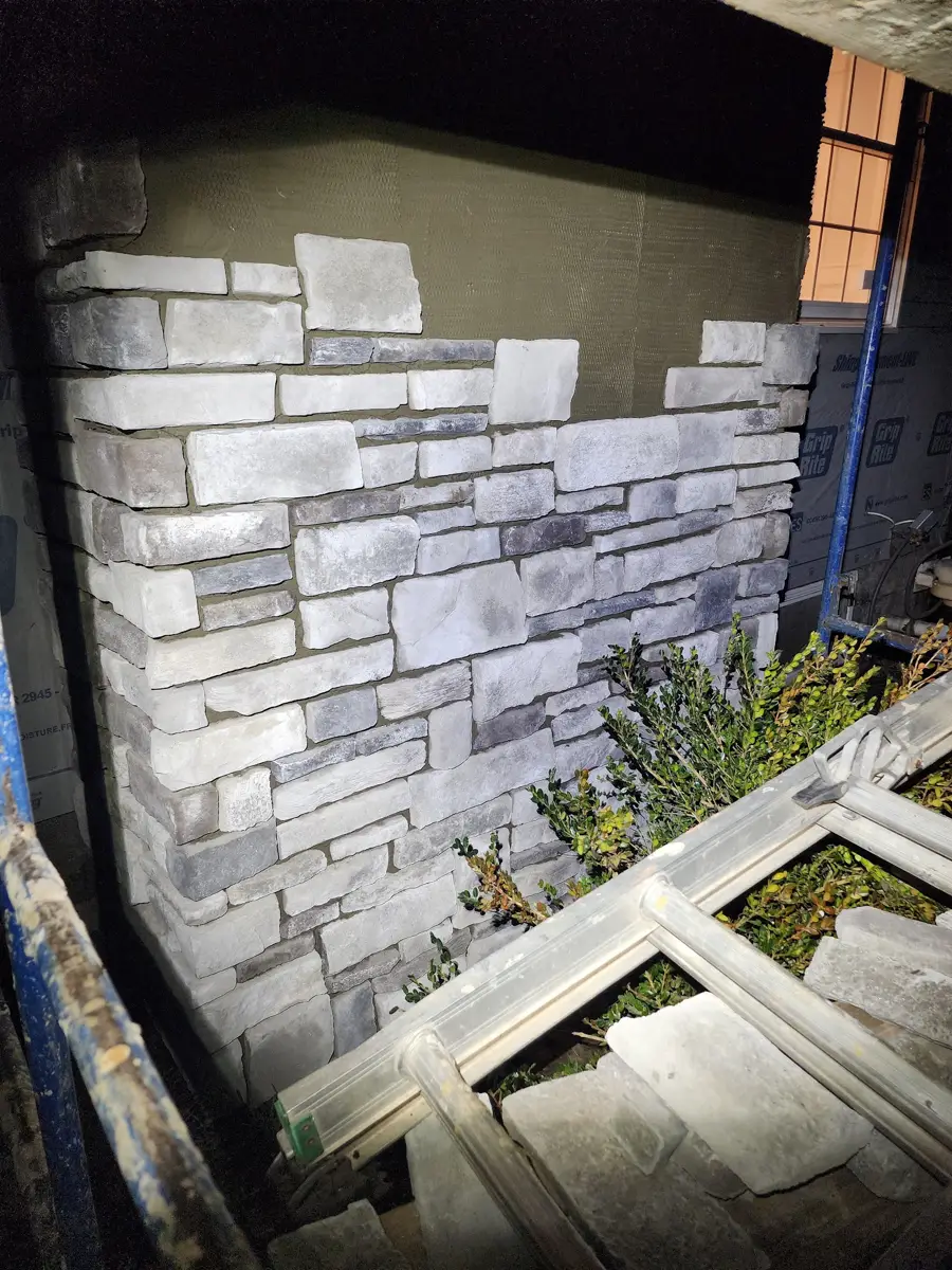 Partially installed gray and white stone veneer on an exterior wall beside scaffolding