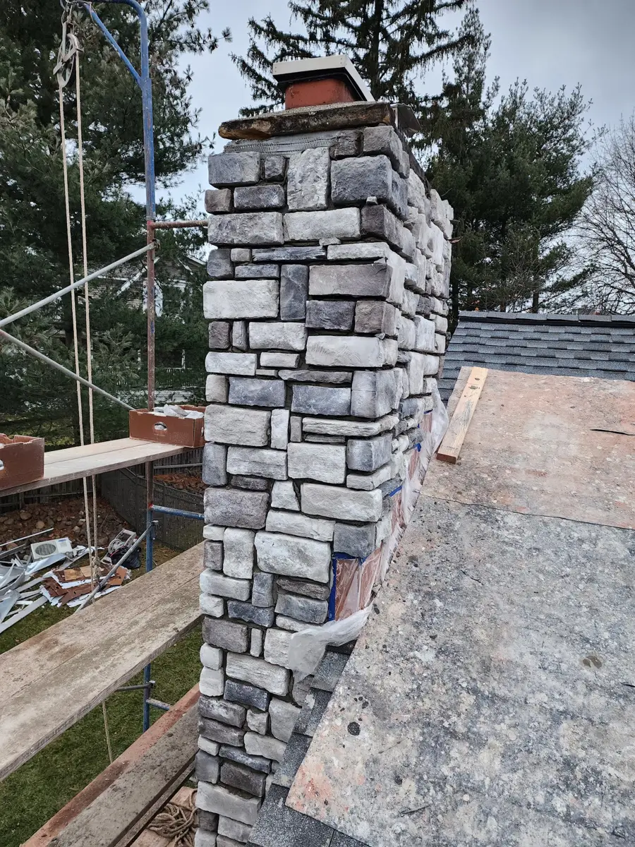 Tall stone-faced chimney seen from the side beside roof scaffolding