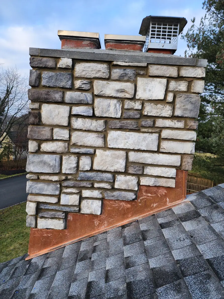 Stone-faced chimney above a shingled roof, with staggered rectangular stones and chimney caps