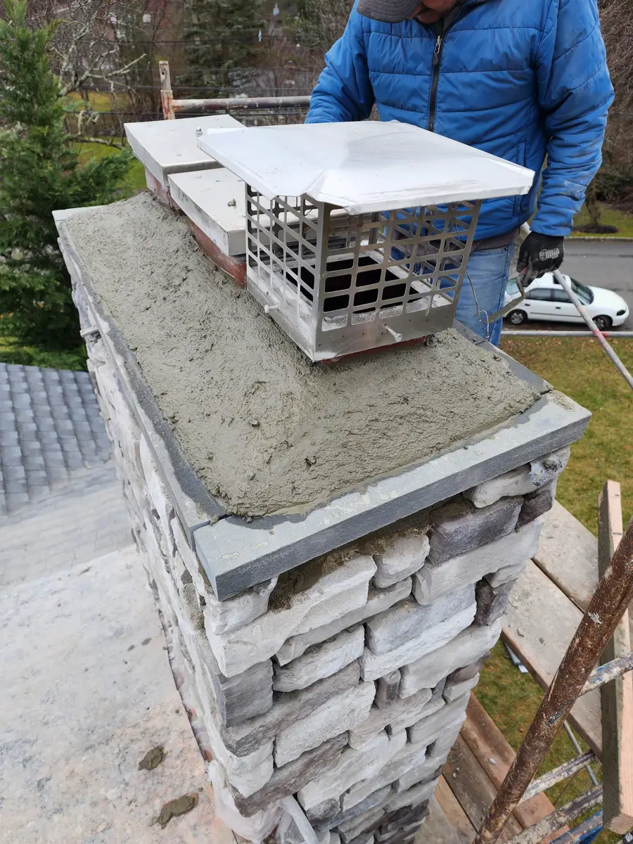 Close view of a chimney cap and wet concrete crown above stone facing